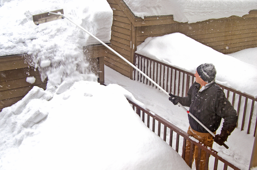 Using a roof rake to remove snow from a home's roof