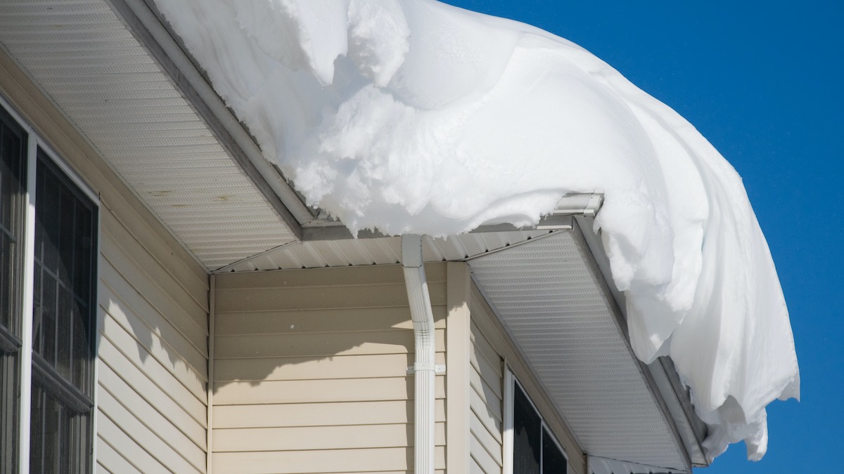 A Snow Drift Atop A Residential Roof, Framed By A Blue Sky