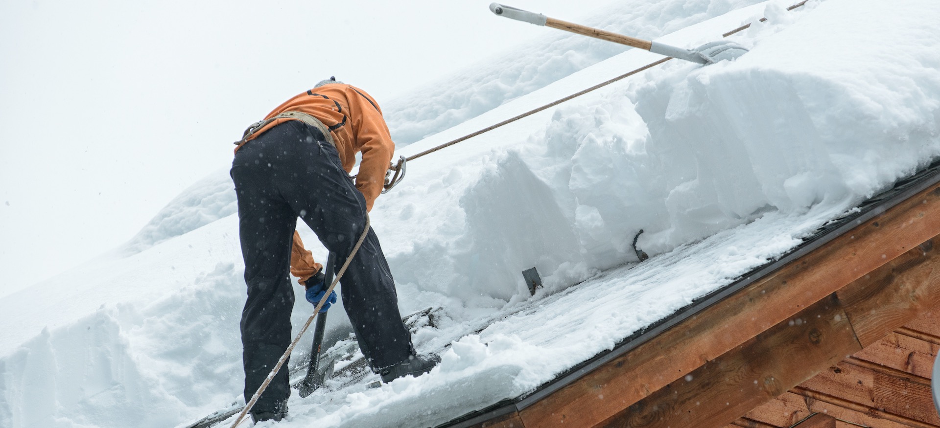Professional roofer removing ice dams and snow from a pitched roof